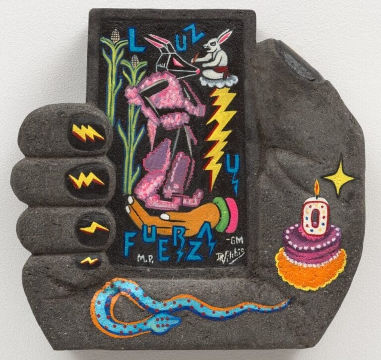 a concrete hand sculpture holding a rectangular form with a birthday cake and o candle, blue snack, symbols, rabbit, and corn painted on it. lightning bolts are painted on the fingernails