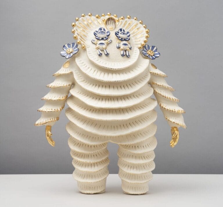 a ceramic figure with a scalloped suit, gold hands, and two floral figures for eyes