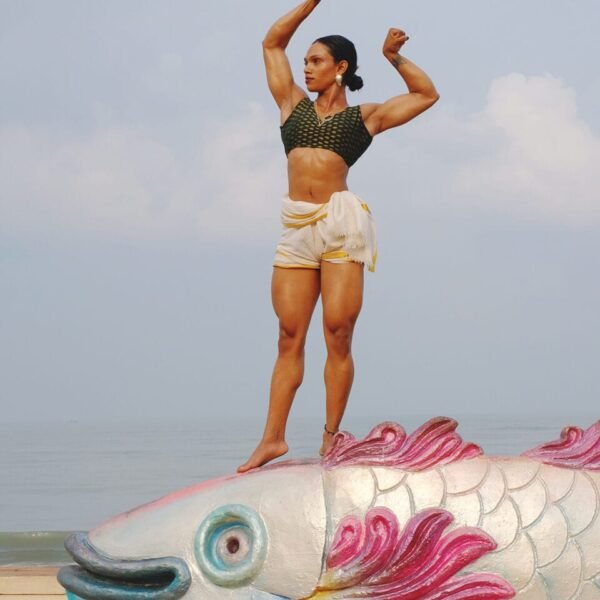 an indian woman in tight shorts and tank top stands atop a fish and flexes