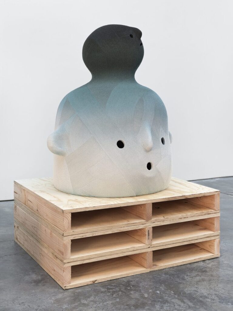 a large ceramic sculpture of a an abstract face in a white-to-black gradient, installed on a pallet-inspired wood pedestal