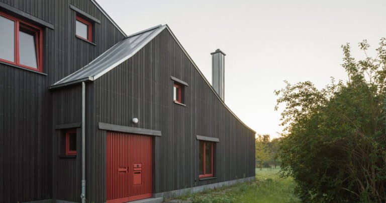 الواجهة الخشبية الداكنة بواسطة KO/OK تتناقض مع البيت الجملون الموجود
