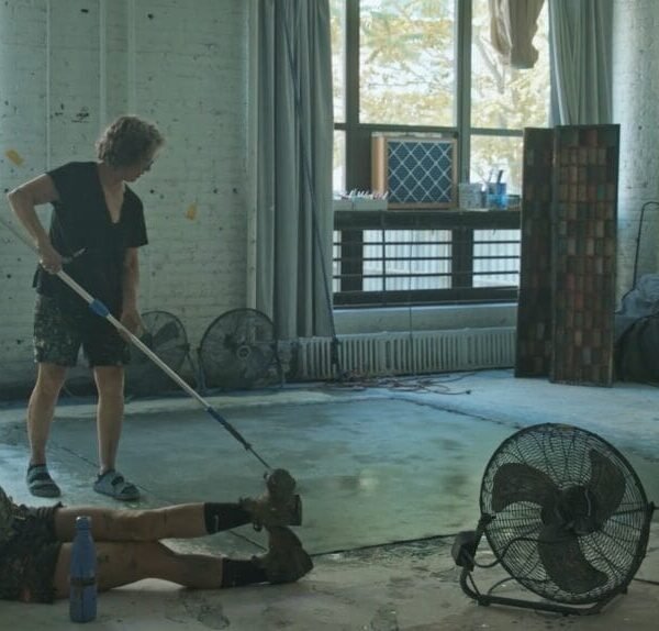 a younger woman sits on the floor while an older woman paints a canvas with a roller
