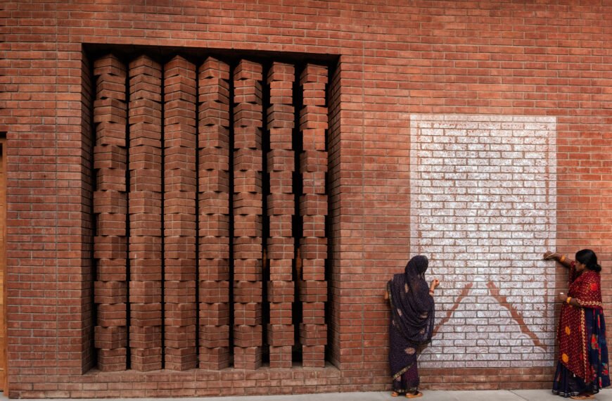 Two women in saris creating a mural on a brick wall