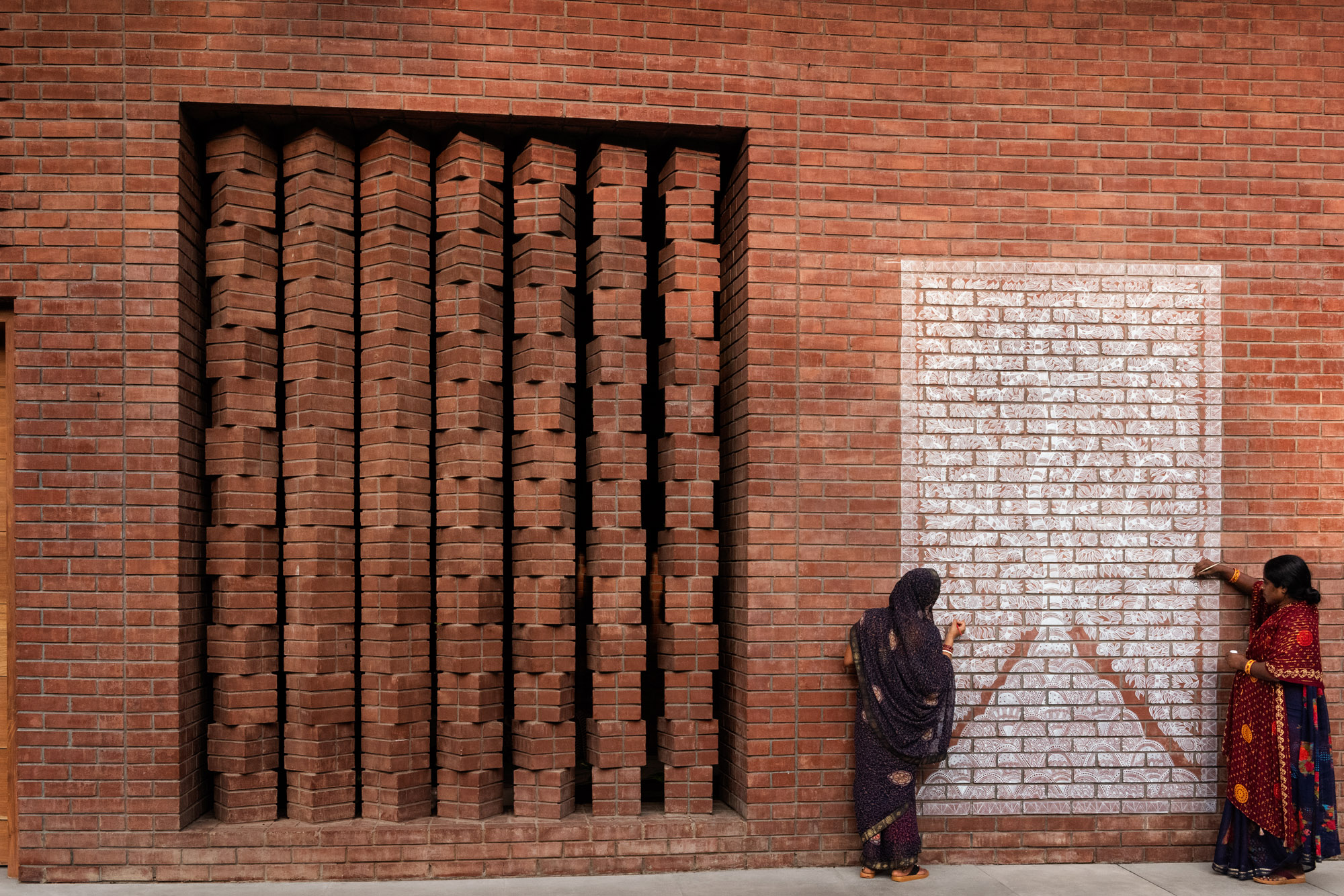 Two women in saris creating a mural on a brick wall