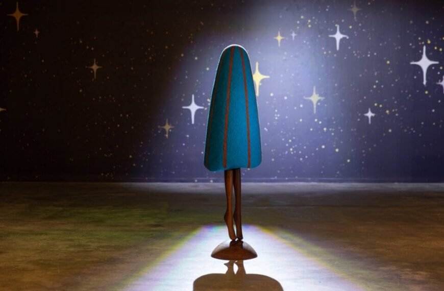 an abstract, colorful, soft sculpture in a darkened gallery installation, with legs as if the form is dancing