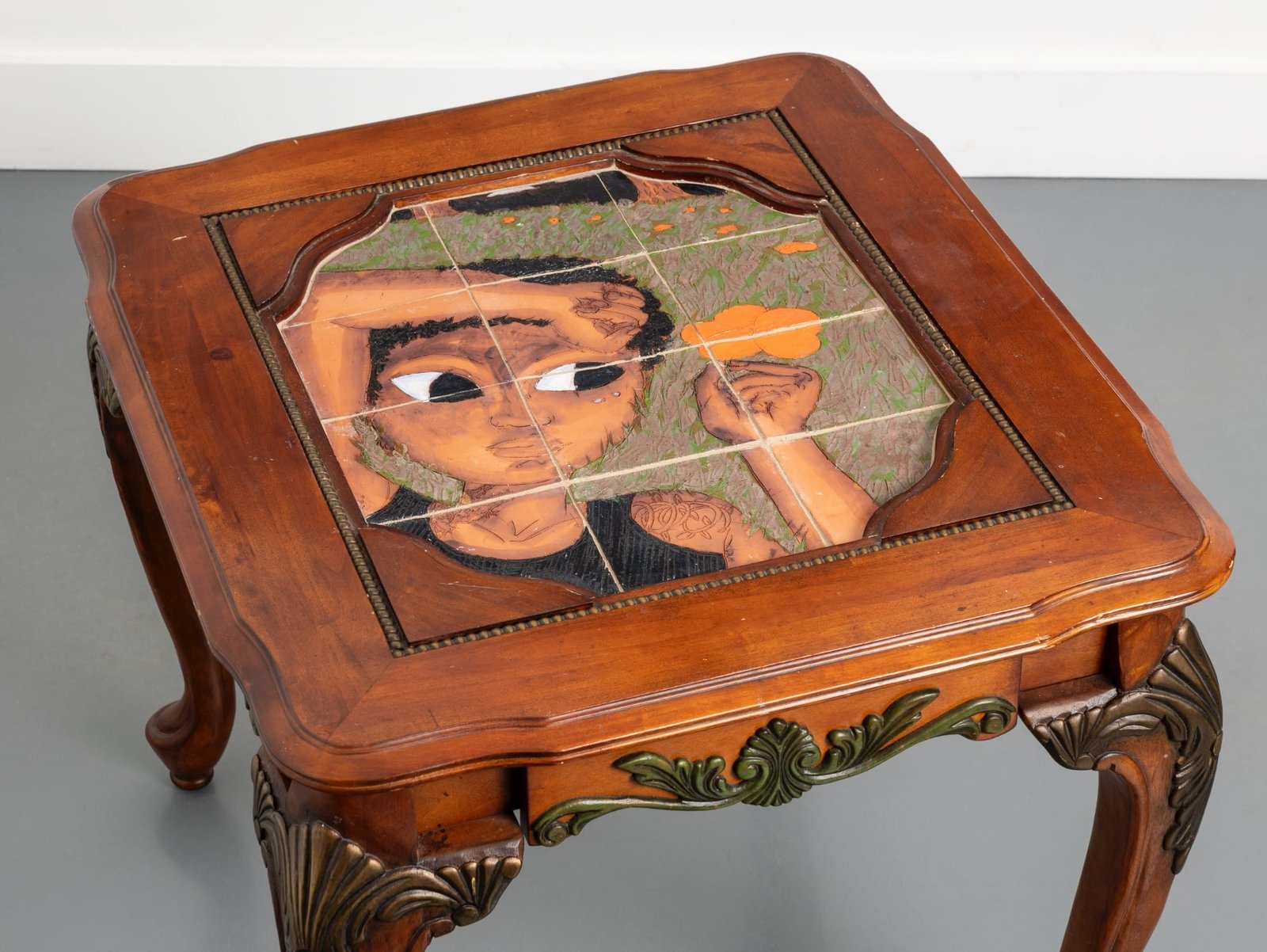 an ornate wood table with a ceramic tile inlay depicting a figure with short black hair holding an orange flower