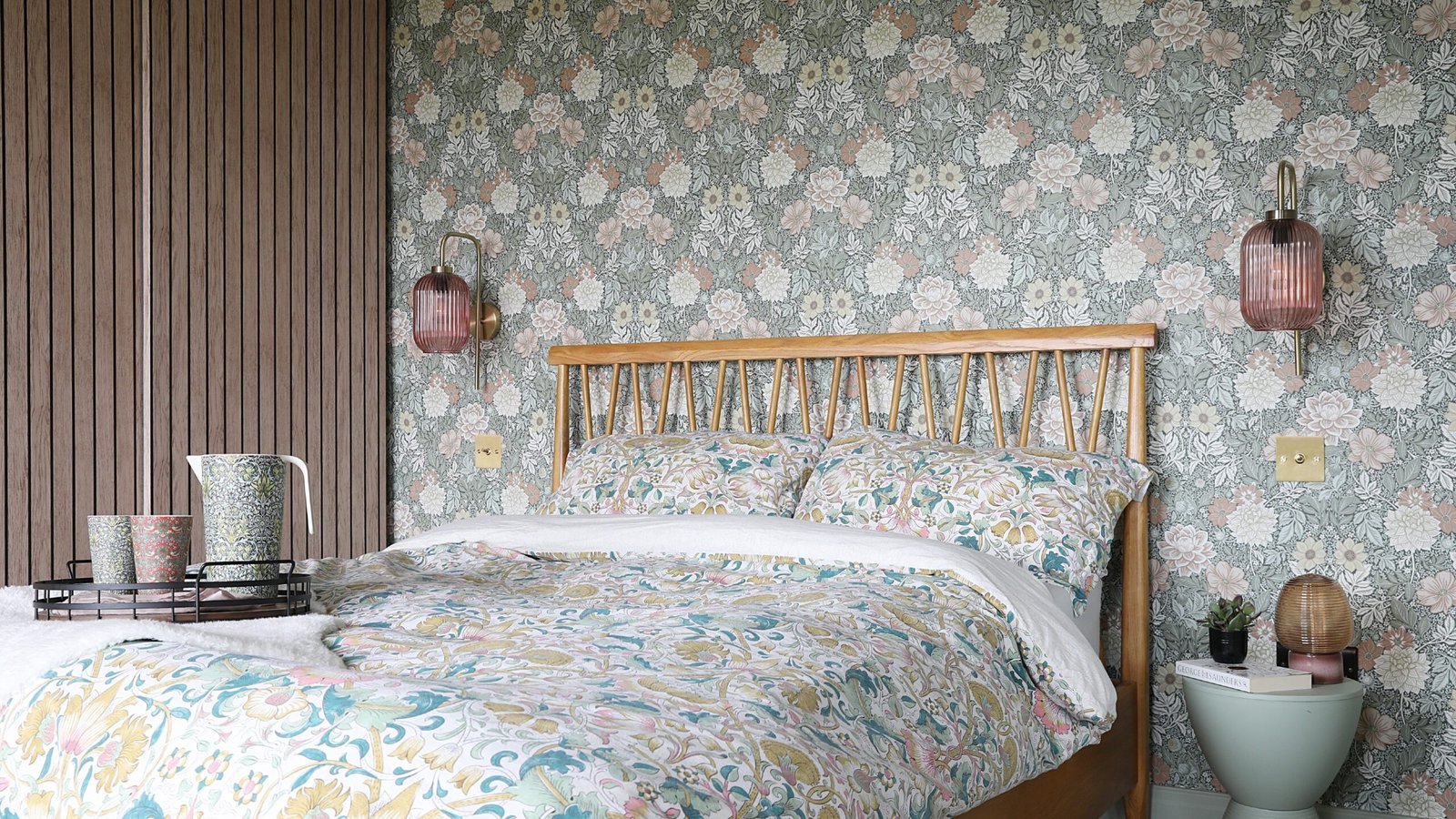 A bedroom with a feature wall behind the bed covered in a floral Morris &amp; Co wallpaper and coordinating Morris &amp; Co bed linen covering the bed