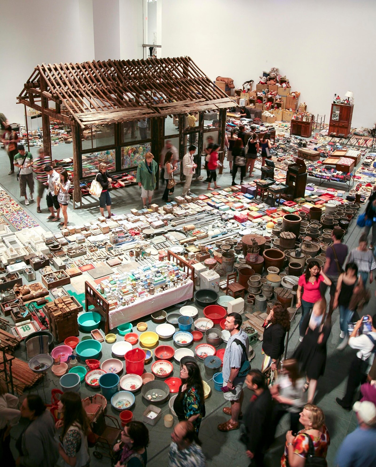 نظرة عامة على معرض وأداء من قبل Song Dong ، توضح الآلاف من العناصر في مساحة معرض جنبا إلى جنب مع هيكل منزل صغير