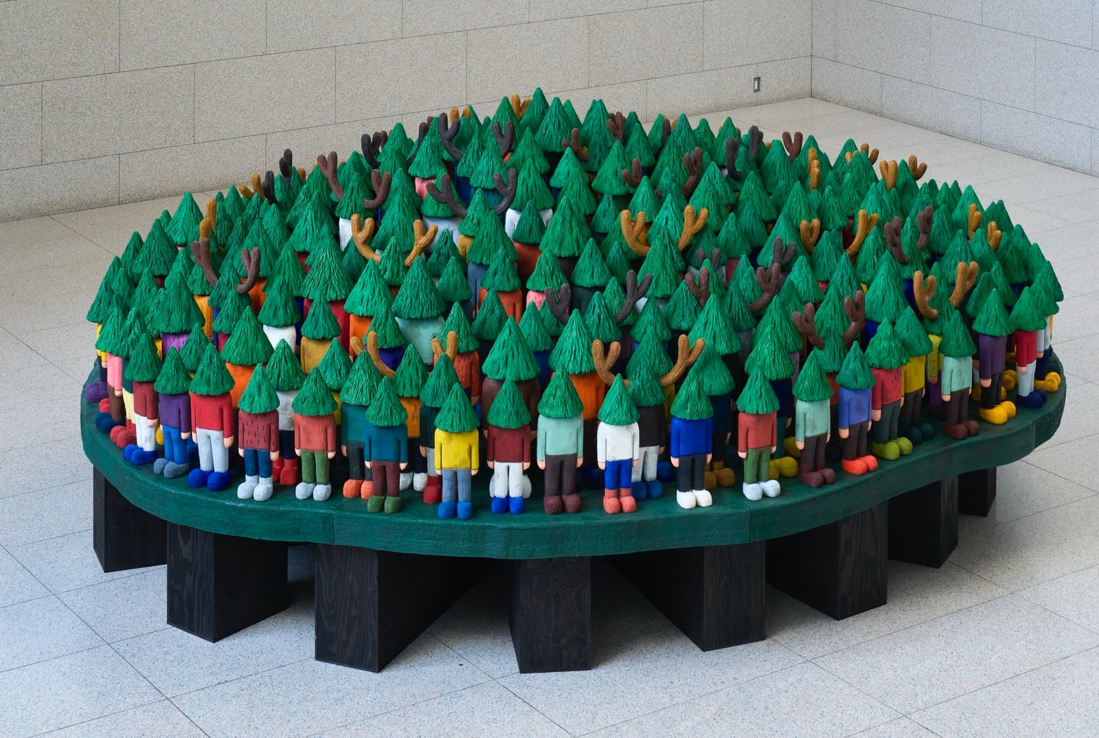 Dream Worlds Emerge in Yuichi Hirako’s Larger-than-Life Domestic Spaces 1 a sculptural installation by Yuichi Hirako of an oversized table covered with cartoonish figures with evergreen trees for heads