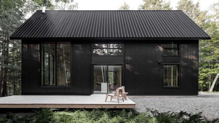 A striking black cottage tucked in a Quebec forest, blending modern design with traditional chalet forms for a moody, minimalist retreat.