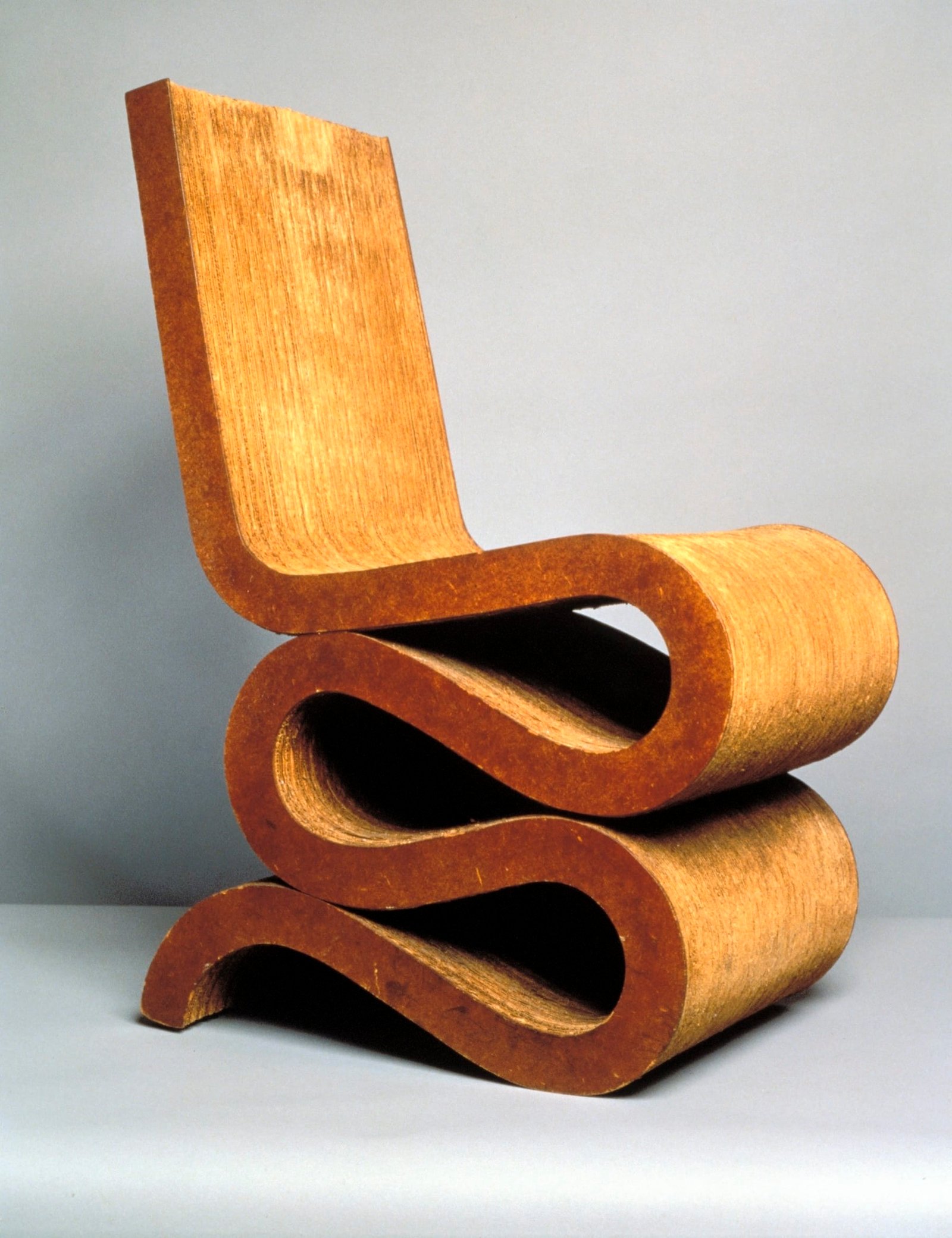 An iconic chair designed by Frank Gehry made from corrugated cardboard that has a straight back and a wiggle shape at the base