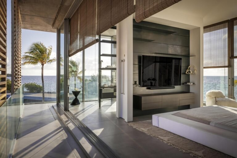 The primary suite features sliding glass walls and textured concrete details with expansive water views.