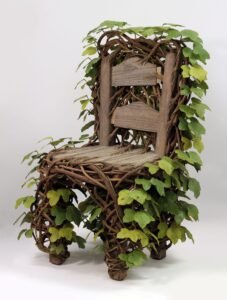 a detail image of a wooden chair with kudzu leaves and roots covering the back and legs by Joyce Lin