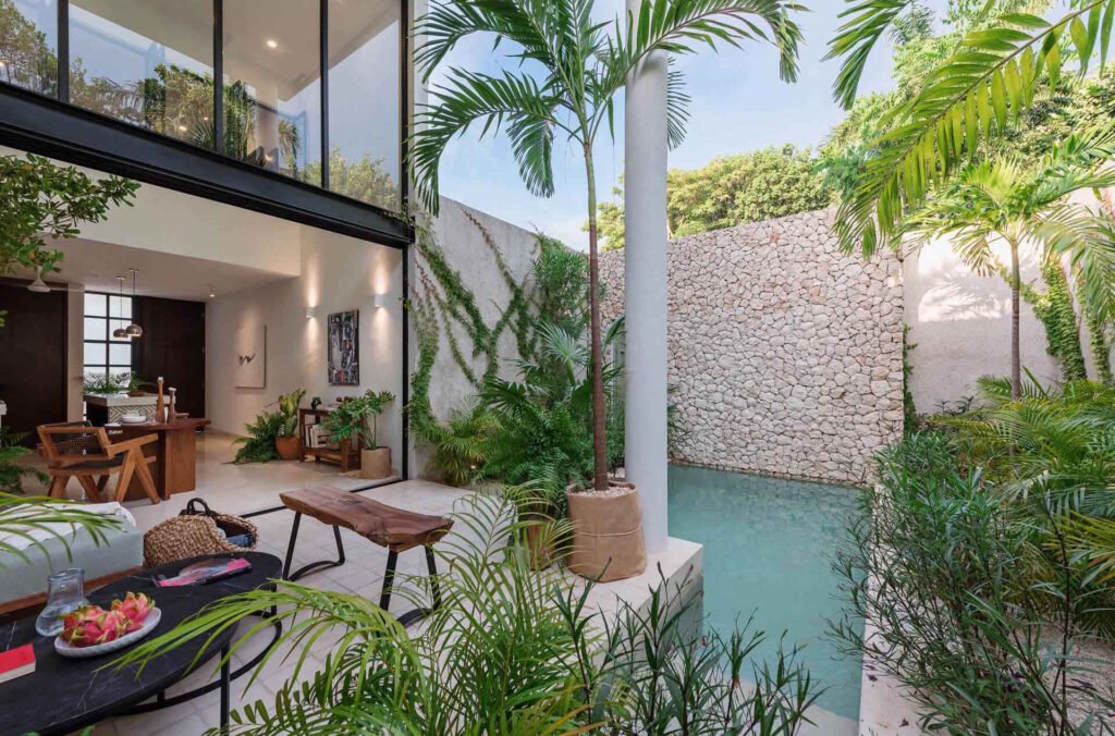 A compact courtyard pool surrounded by tropical plants and a textured stone wall creates a peaceful place to cool off on warm days.