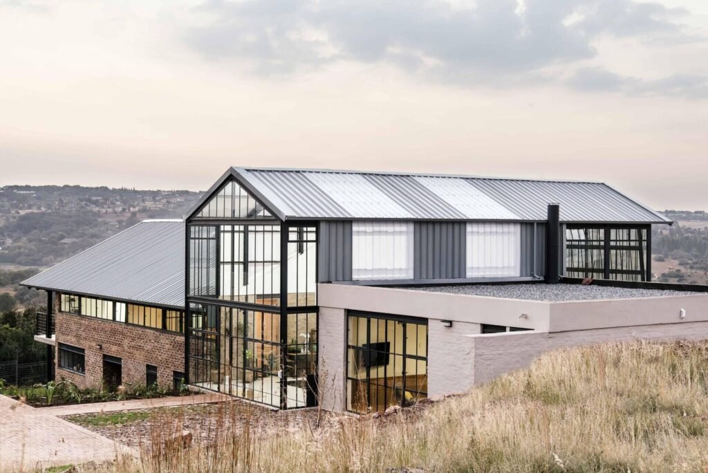 Cement-washed brick, steel, and concrete create a low-maintenance exterior with a strong, modern edge. A double-height conservatory with openable walls and a glass floor becomes the heart of this light-filled home.